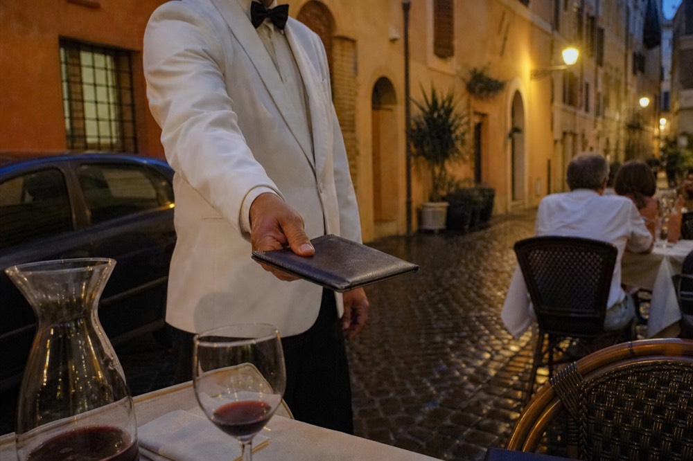A waiter presenting a leather bill folder in a Roman restaurant