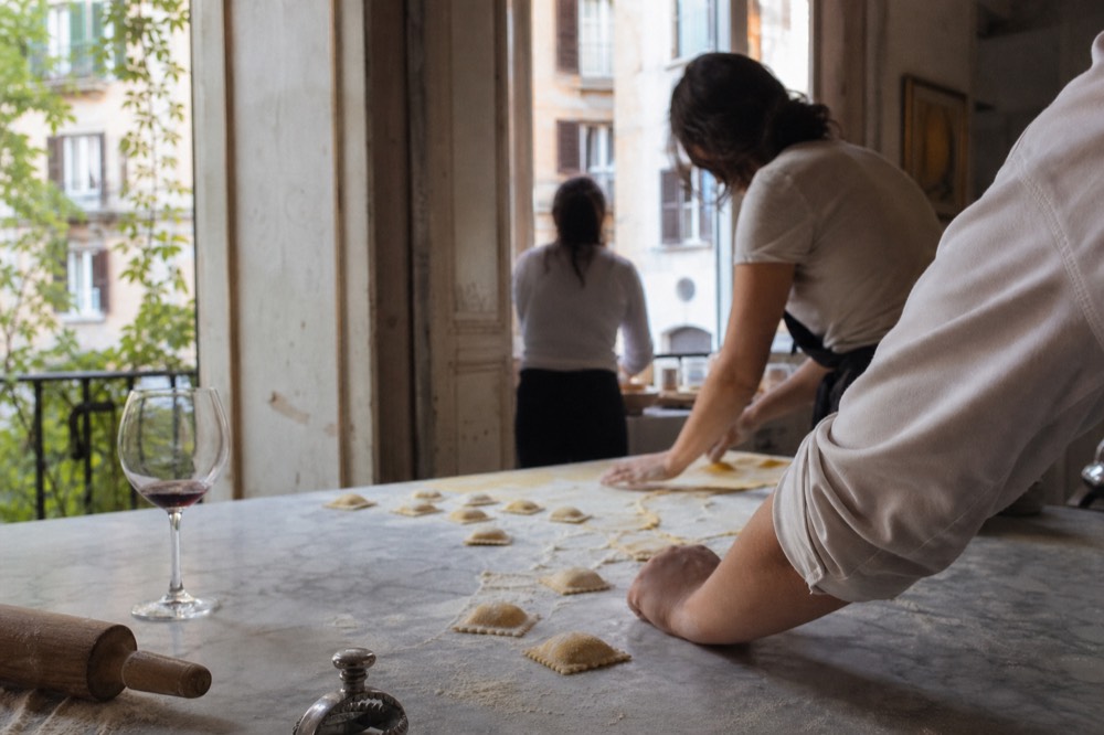 Hands shaping fresh ravioli on a floured marble counter