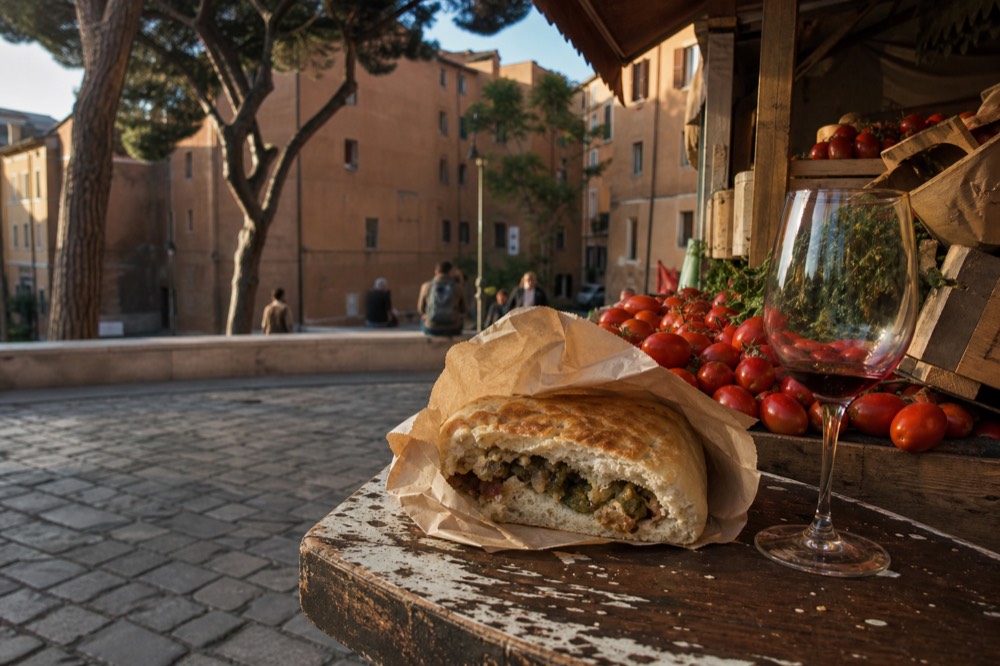 A filled bread pocket wrapped in paper on a wooden counter beside a market stall