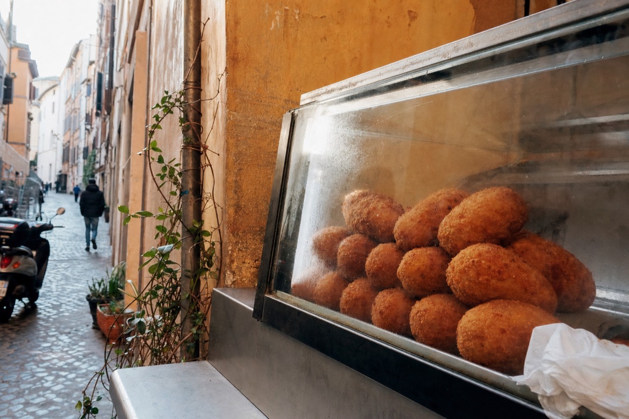 Golden fried rice balls stacked in a glass display case at a Roman street food counter
