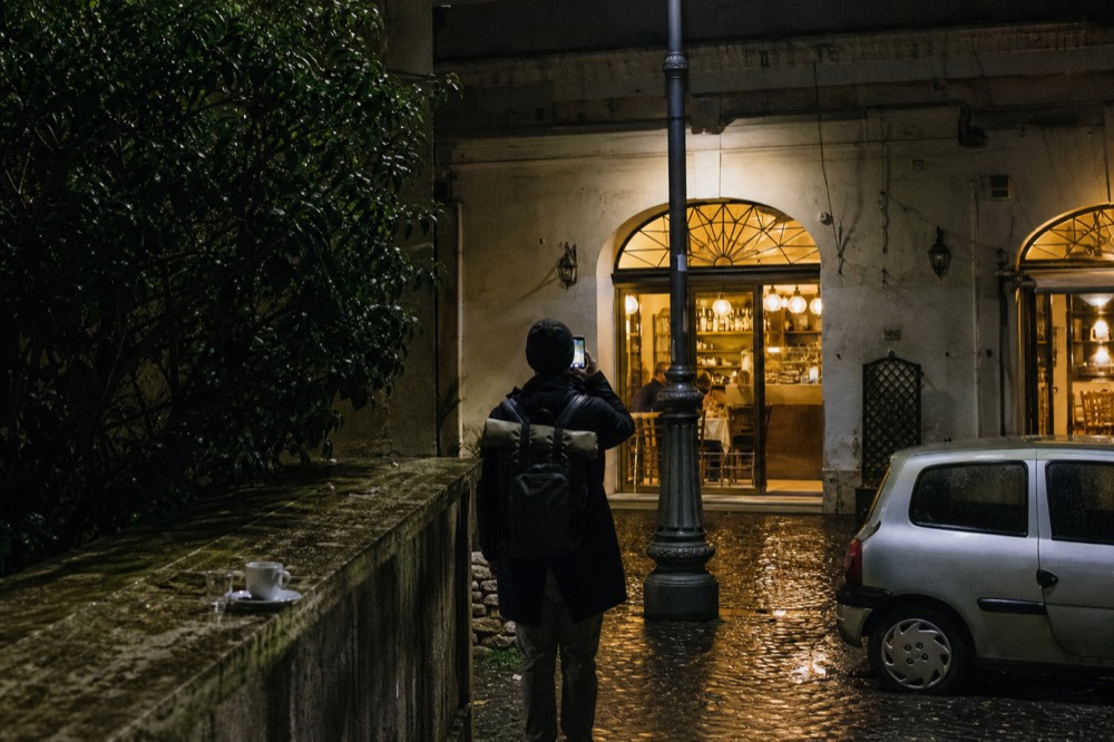 A phone screen showing an online restaurant booking page in a Roman street at night