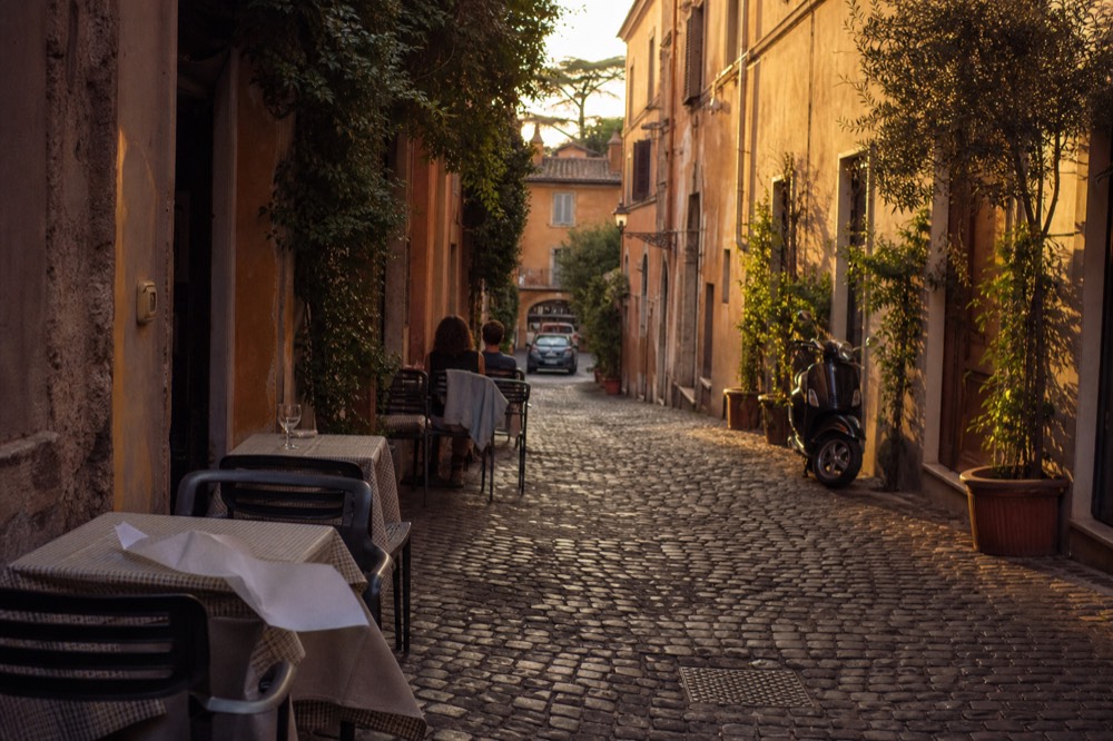 Golden evening light on a narrow Rome street with cafe tables set outside