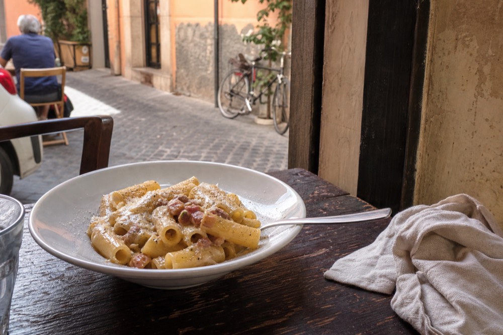 Rigatoni carbonara in a white bowl on a rustic trattoria table