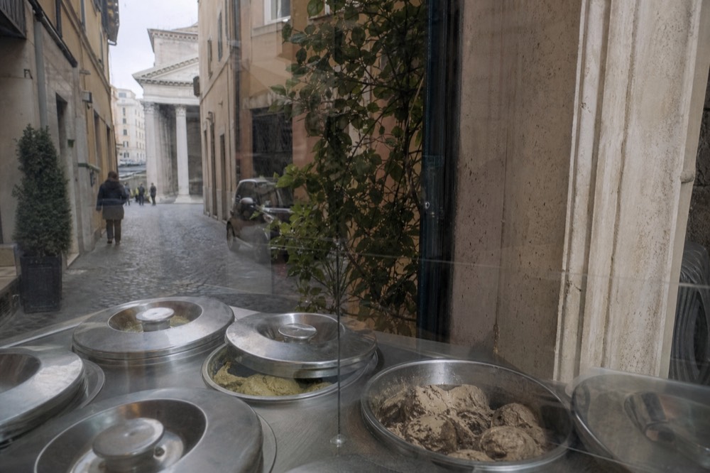 A close view of covered metal gelato tins behind a glass counter in Rome