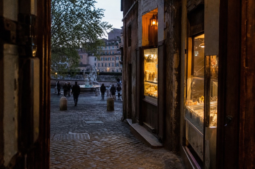 An evening street in Trastevere with food counters and a gelato window