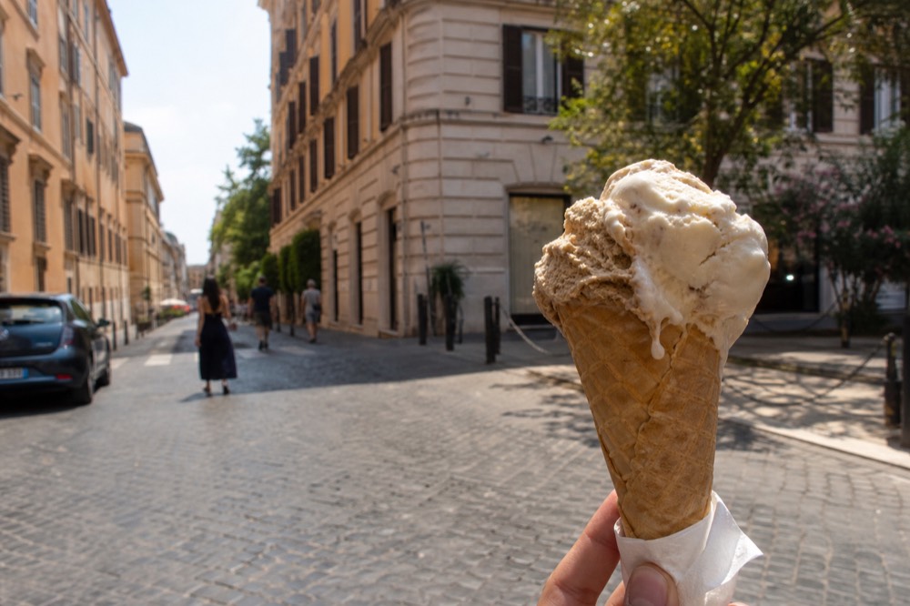 A cone of natural muted-coloured gelato against a Roman street backdrop