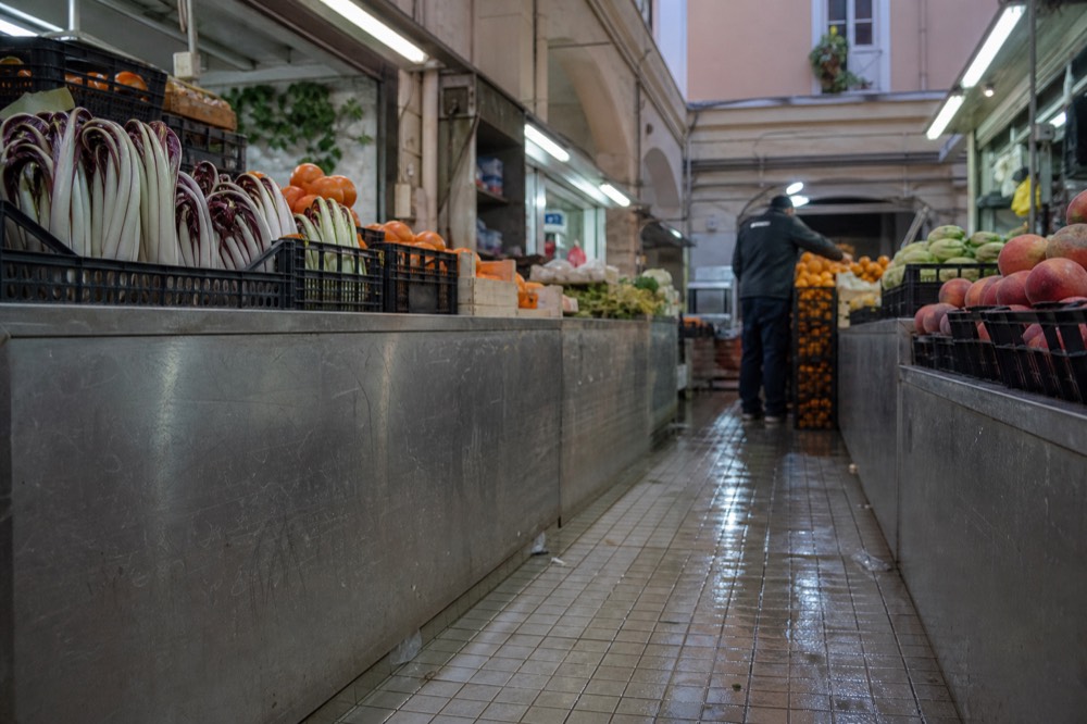 A covered market aisle with produce stalls under fluorescent light