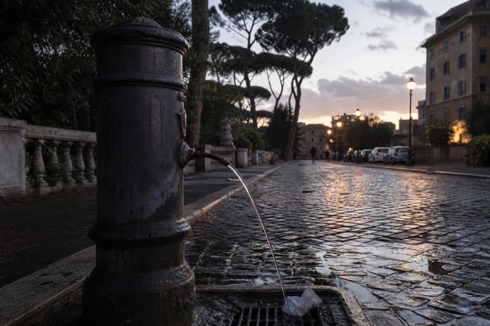 A cast-iron drinking fountain running water onto Roman cobblestones