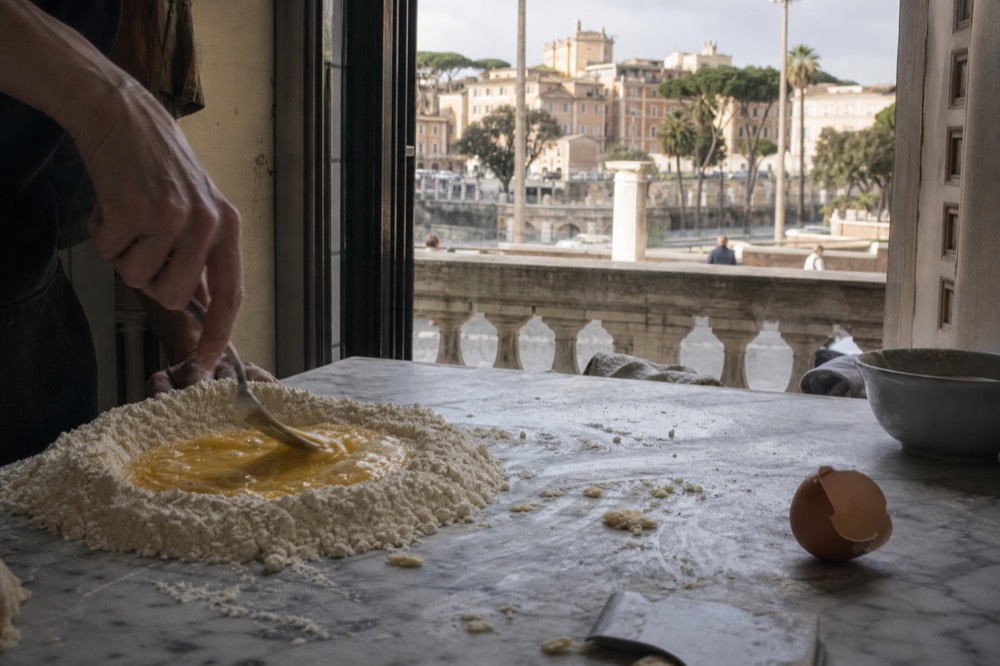 A marble worktop with eggs, flour and a fork for making fresh pasta dough