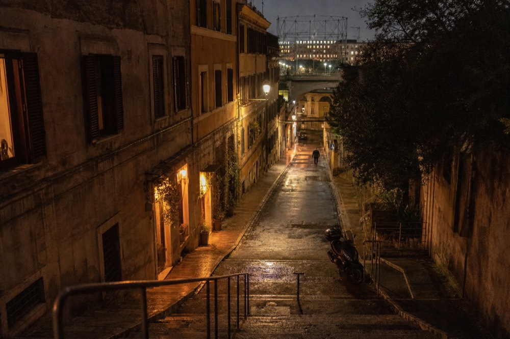 A Roman street corner at night with warm light from small eateries