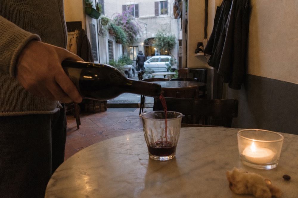 A candlelit table in a Trastevere wine bar with red wine being poured