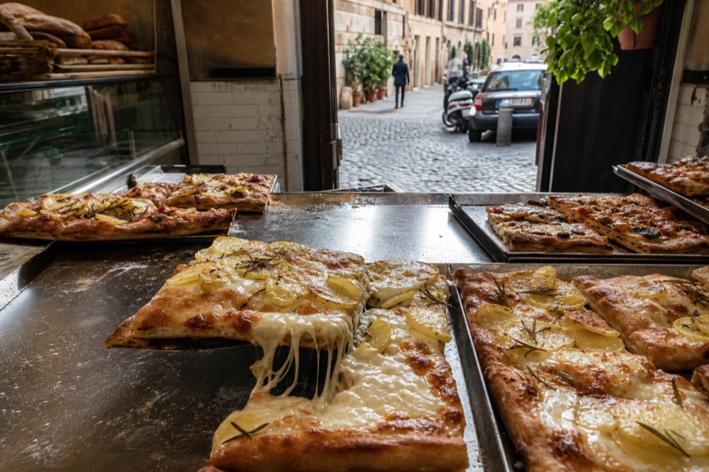 A counter of pizza al taglio trays in a Roman bakery