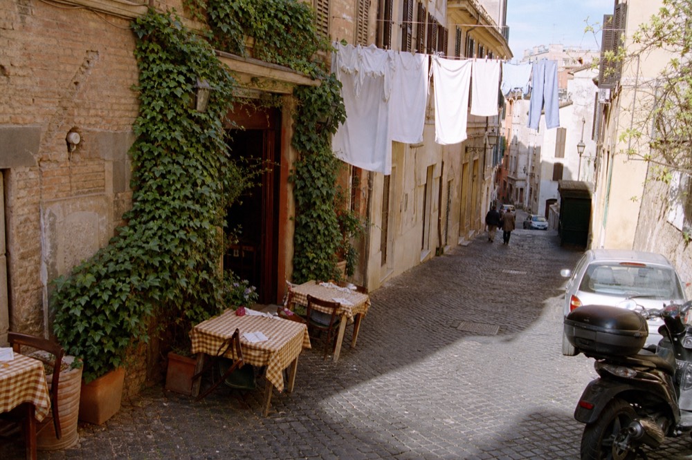 A narrow cobbled street in Monti with a few tables outside a trattoria